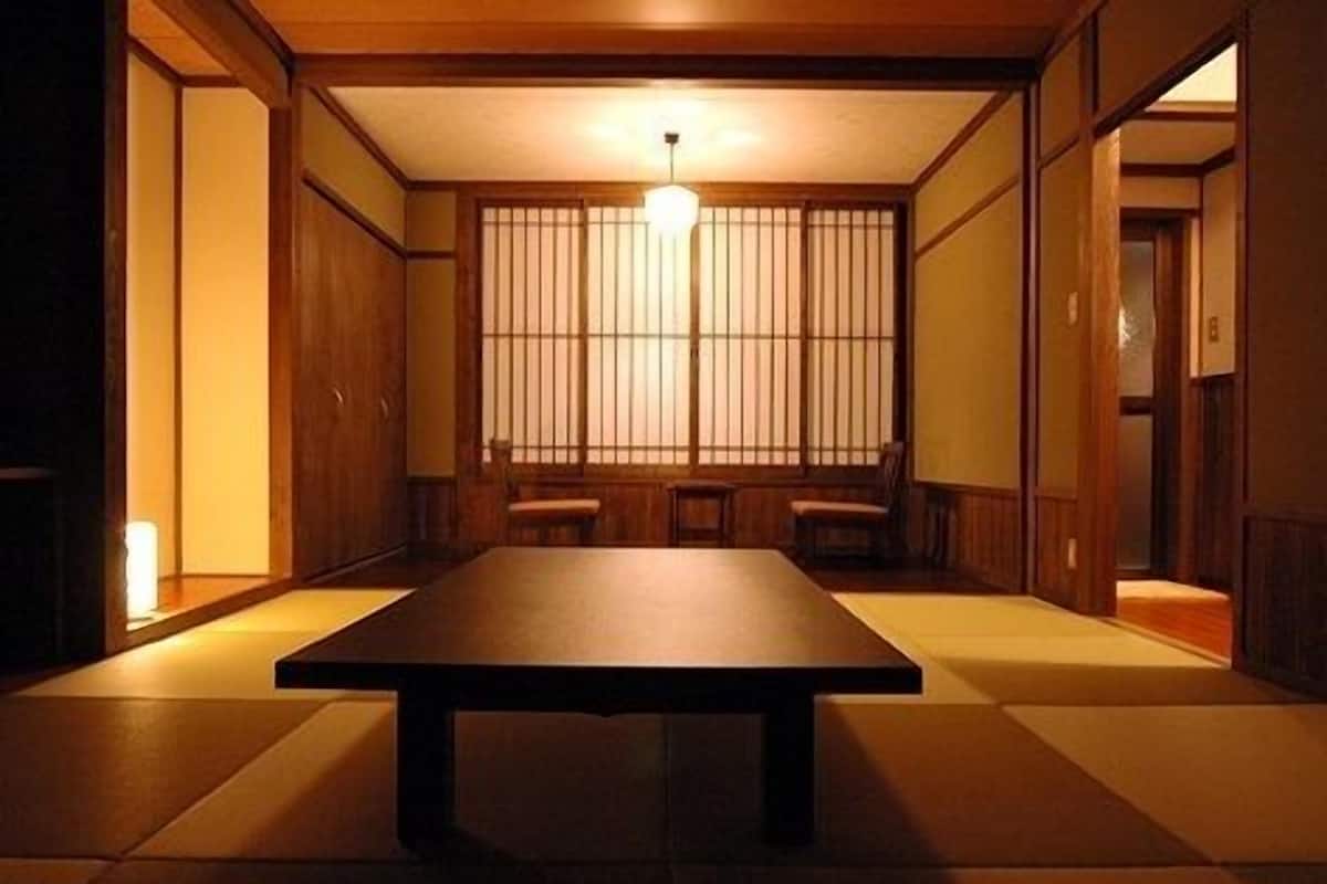 Une pièce de style japonais traditionnel, avec un sol recouvert de tatamis, une table basse, des portes coulissantes et un luminaire suspendu.
