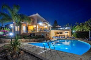 Une maison à deux étages avec une piscine, un espace salon extérieur et un balcon bien éclairé.