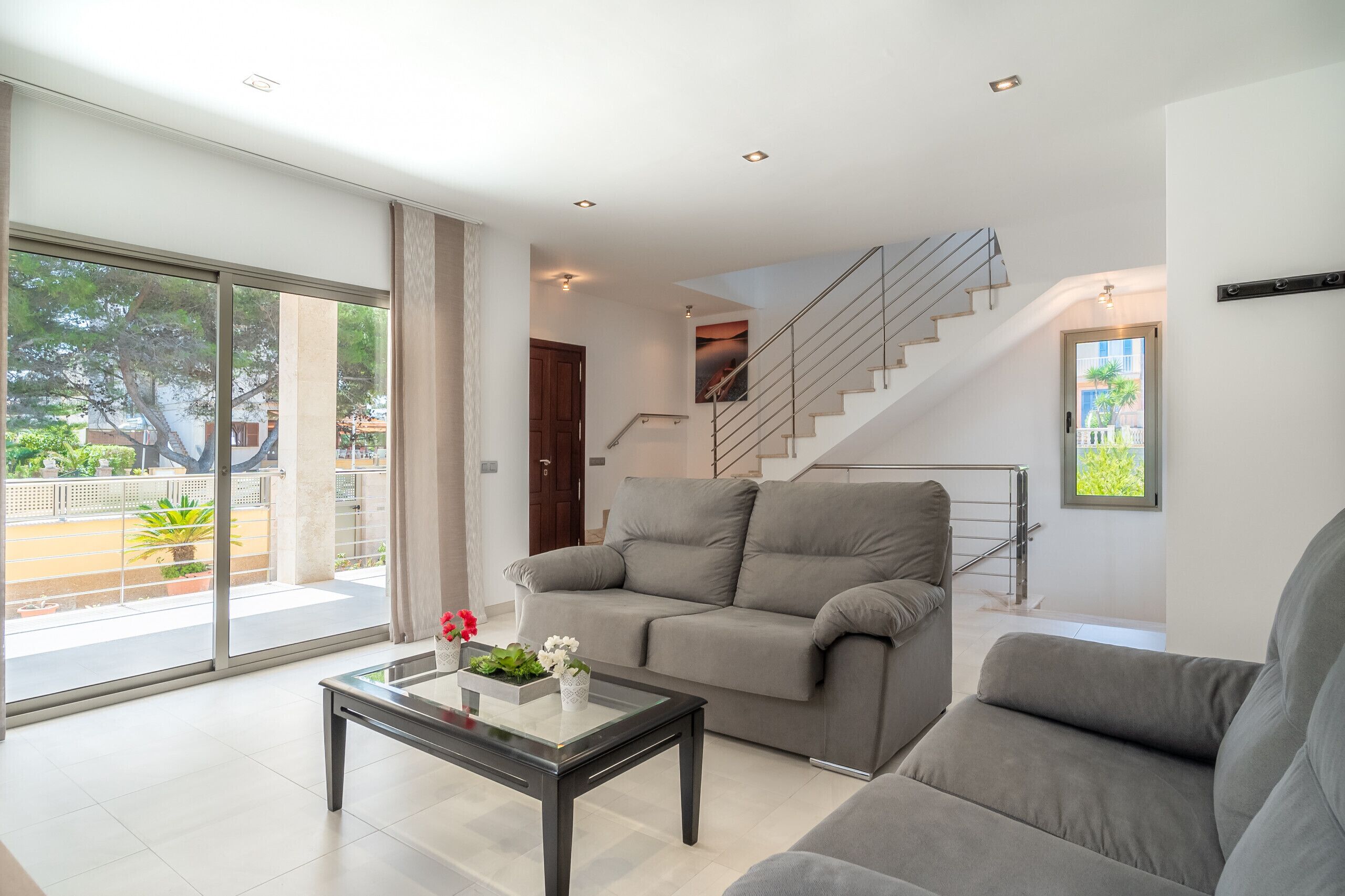 Ein modernes Wohnzimmer mit einem grauen Sofa, einem Glastisch und einer Treppe, die zu einer oberen Etage führt.