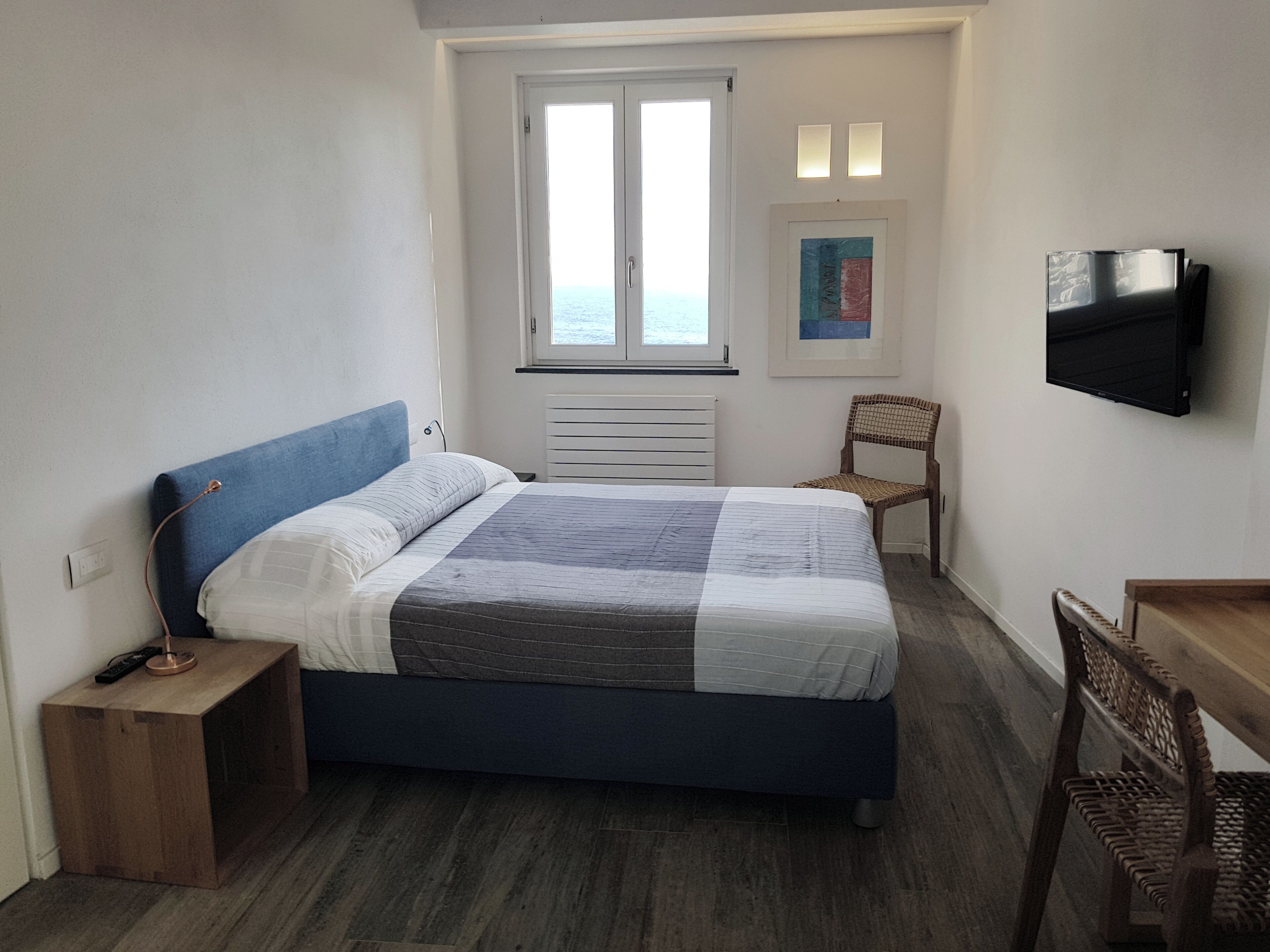A bedroom with a bed, a wooden nightstand, a chair, a TV, and a window with a view.
