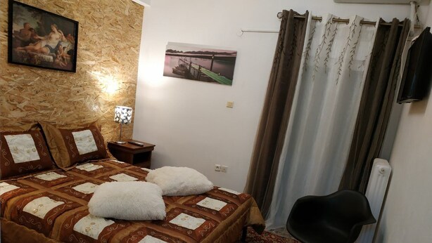A bedroom with a large bed, a nightstand, a chair, and a painting on the wall. - Sweet Home Apartment in the center of the city (Korinthos)