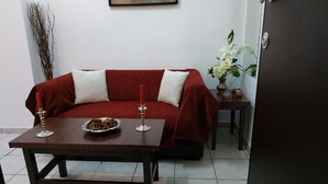 A living room with a red sofa, two white cushions, a dark wooden coffee table with a plate of food and two red candles. - Sweet Home Apartment in the center of the city (Korinthos)