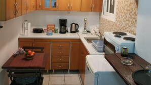A compact kitchen with wooden cabinets, a dining table with chairs, a coffee maker, and a stove. - Sweet Home Apartment in the center of the city (Korinthos)
