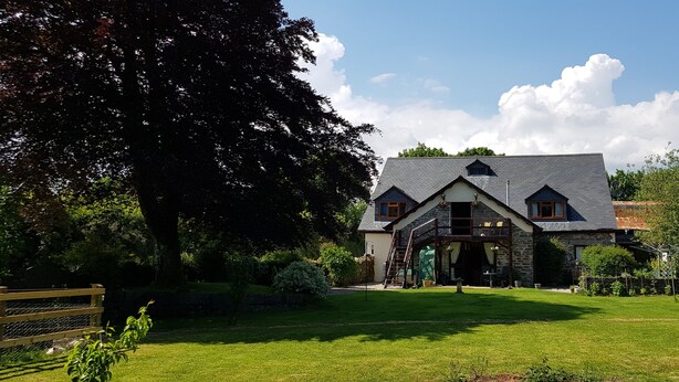A two-story stone house with a sloped roof, a wooden deck, and a well-maintained lawn.