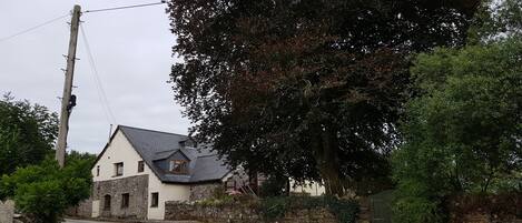 Eine ländliche Straße mit einem Steinhaus, das ein geneigtes Dach und einen großen Baum im Hintergrund hat.