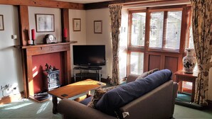 A living room with a sofa, a wooden coffee table, a television, a fireplace, and a window with blinds.