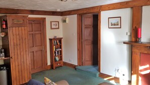 A cozy room with wooden doors, a bookshelf, a small trash bin, and a red candle on a shelf.