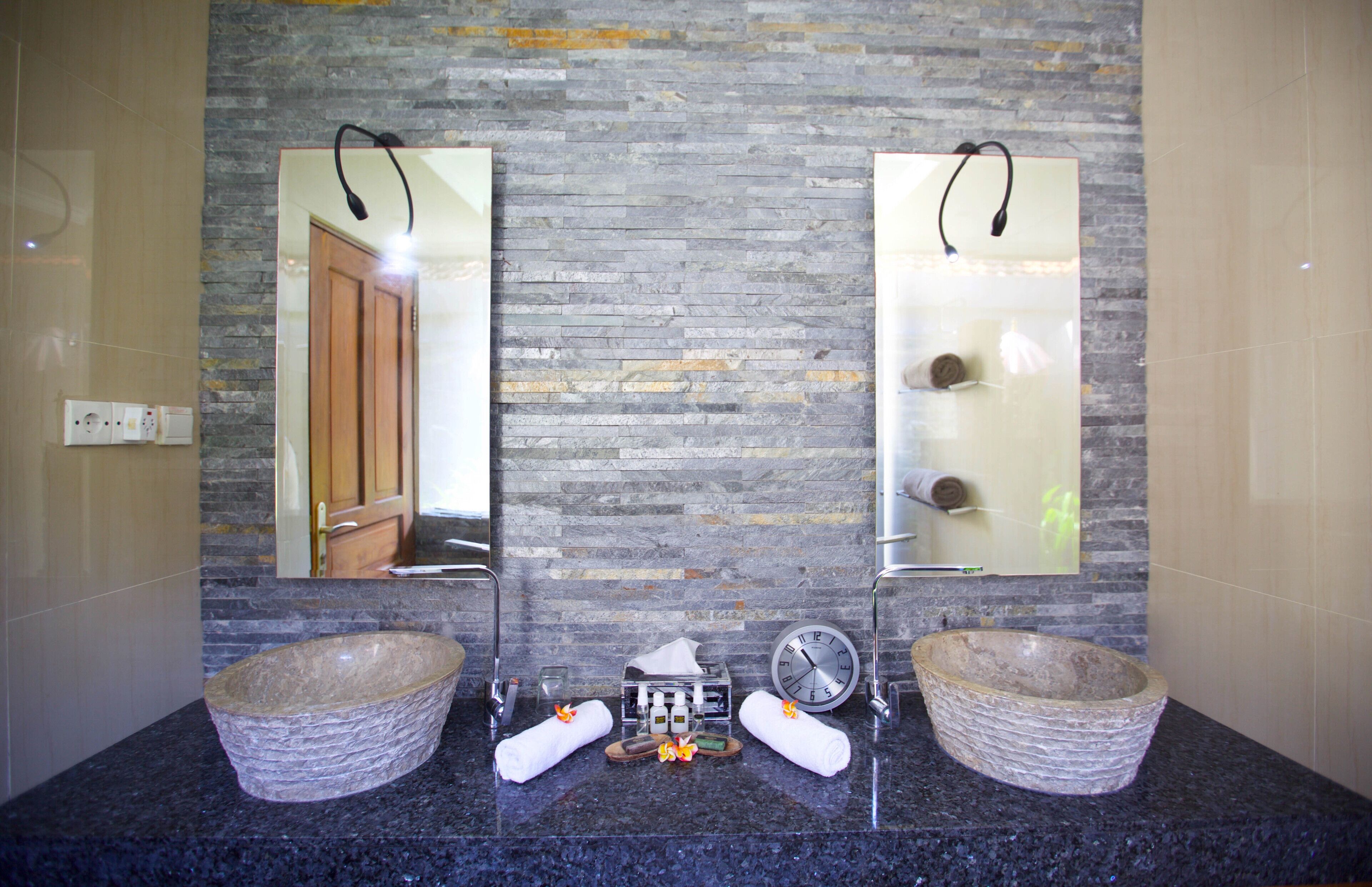 A bathroom with two stone basins, a clock, and a towel rack.