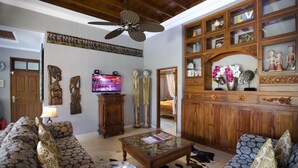 Uma sala de estar com sofá, mesa de centro, televisão e um armário de madeira com portas de vidro.