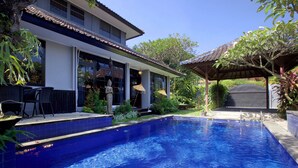 Piscina com borda azulejada, área de pátio coberta e mobiliário de exterior.