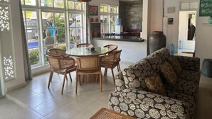 Uma sala de estar ampla com uma mesa de jantar e cadeiras, um sofá estampado e grandes janelas com vista para o exterior.