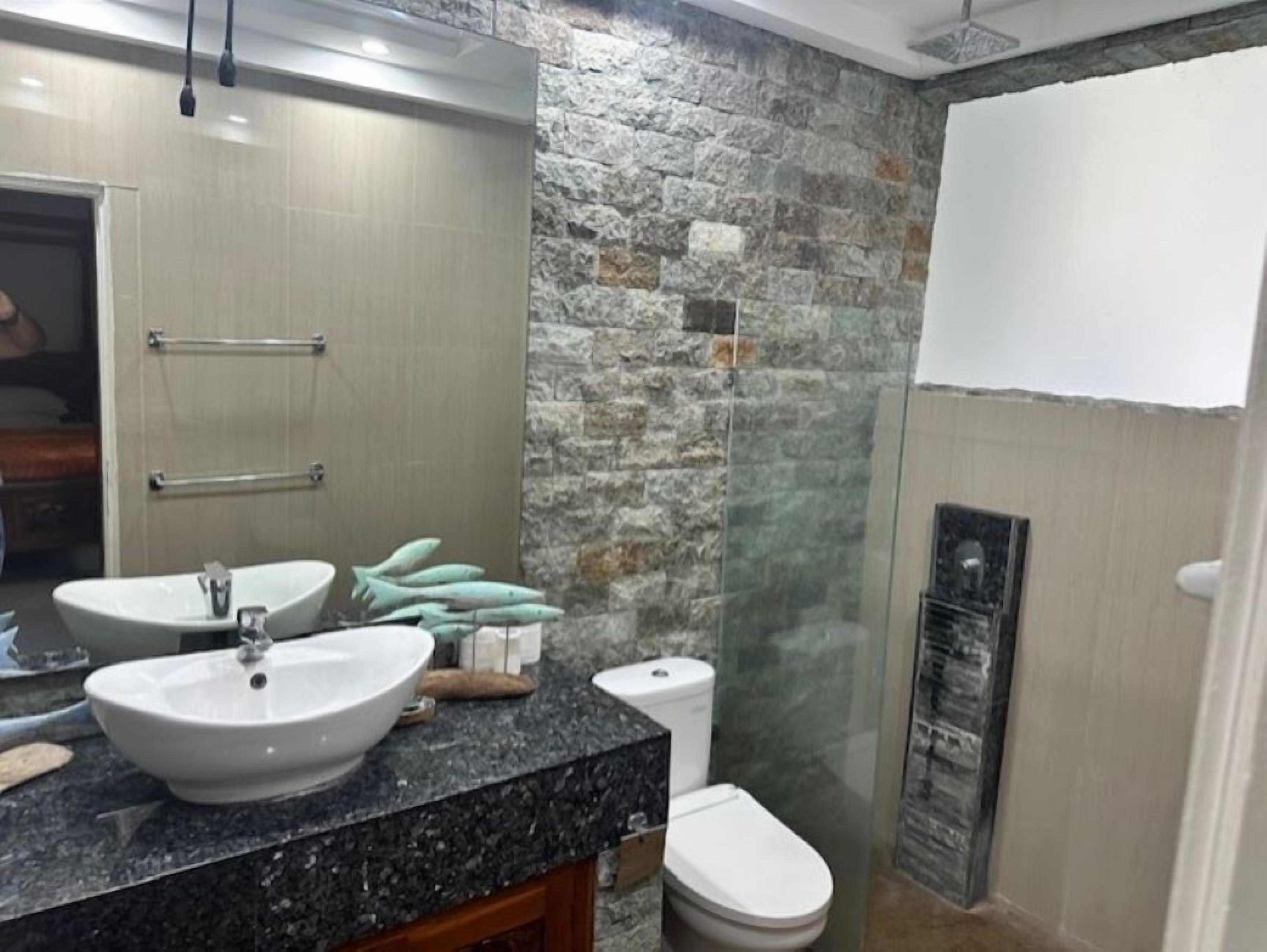 A bathroom with a granite countertop, two sinks, a toilet, and a glass shower enclosure.