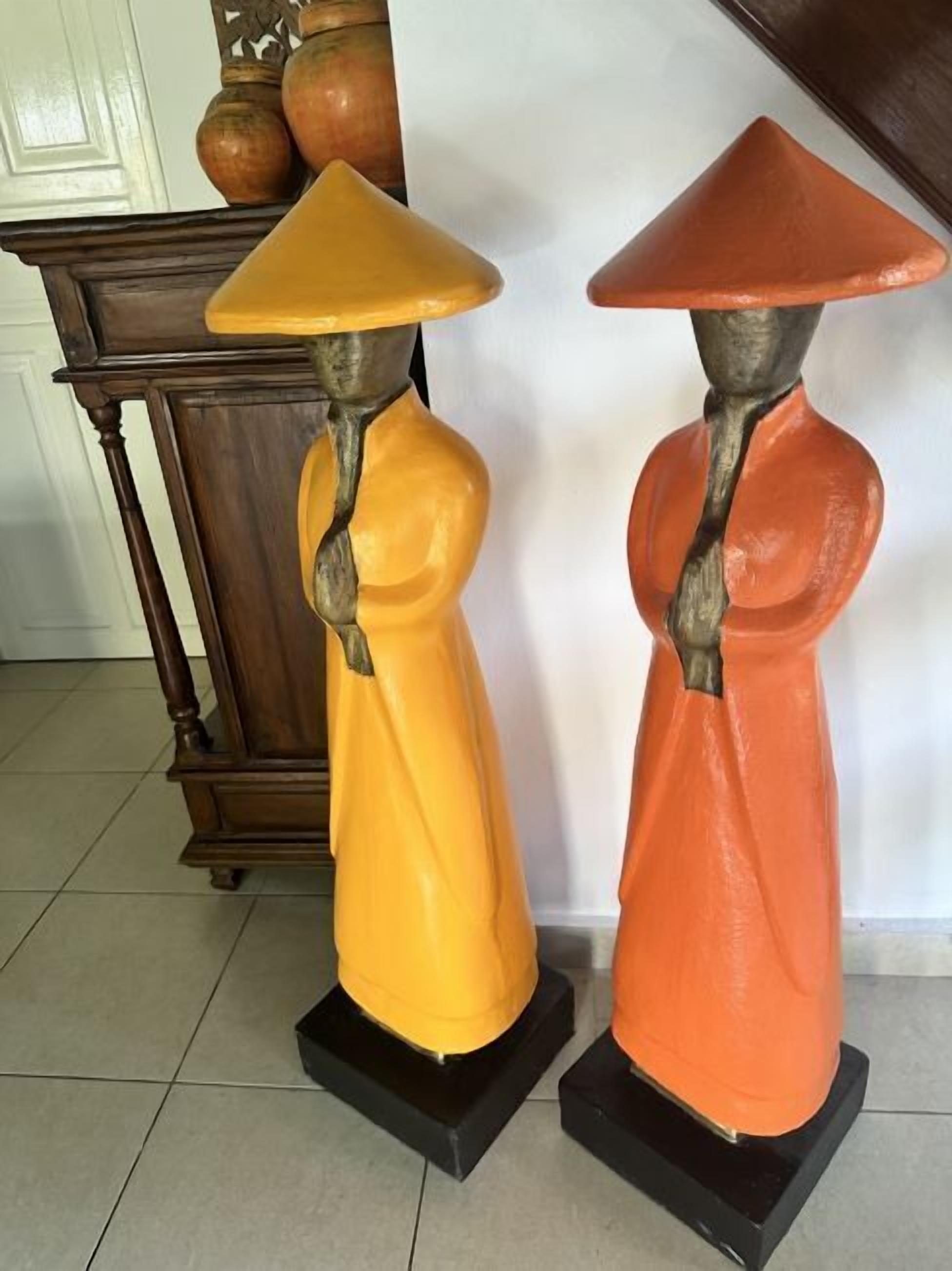 Due statue raffiguranti figure con cappelli conici su piedistalli neri.