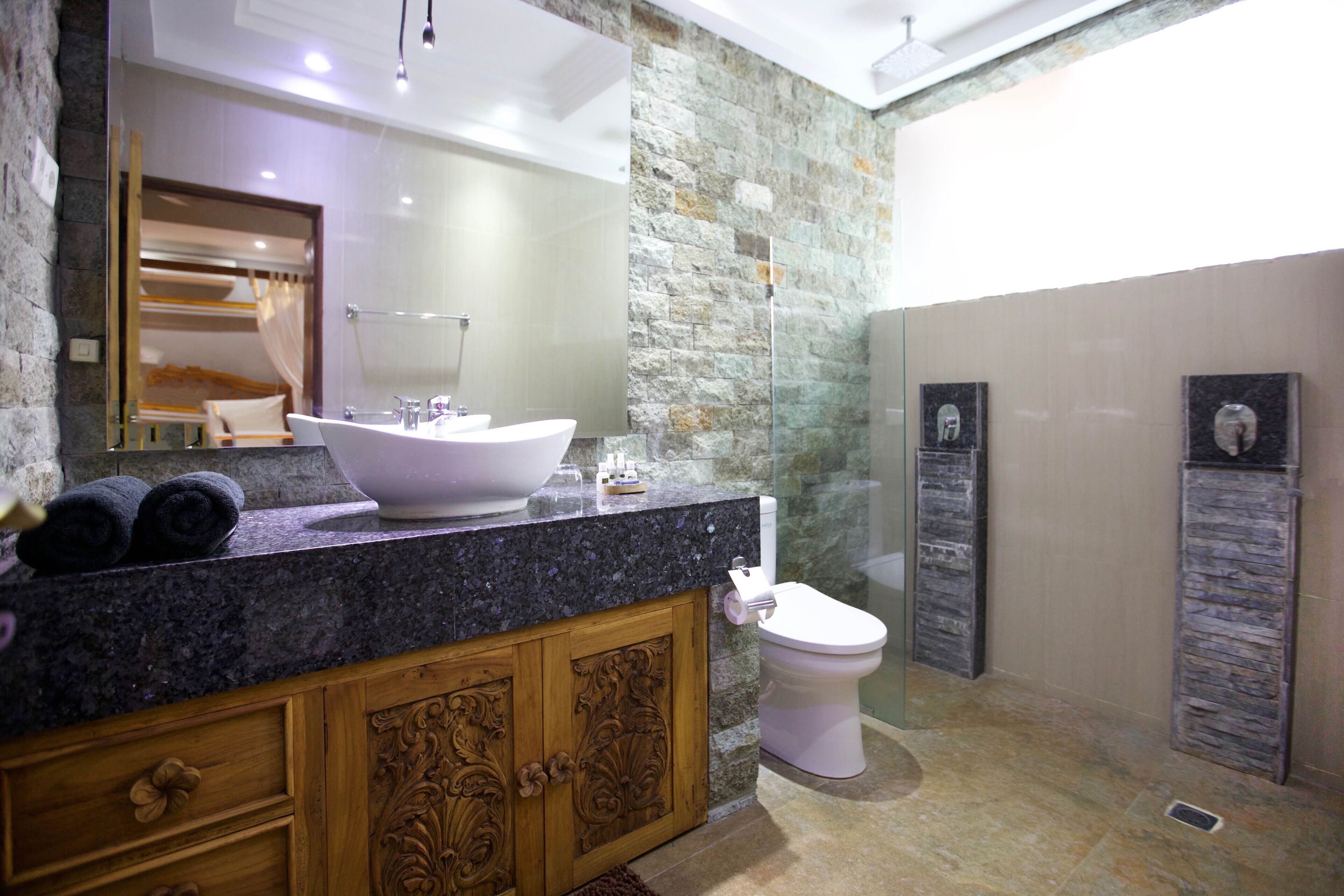 A bathroom with a stone wall, a large sink, a toilet, and a shower area.