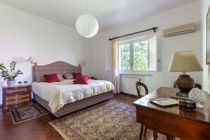 A bedroom with a bed, bedside tables, a desk, a chair, a window, and a hanging light fixture. - Domus Sicily - Il Giardino di Michela - Heated Pool (Palermo)