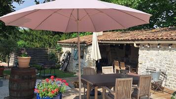 Une terrasse extérieure avec une table et des chaises, un grand parasol et un mur de pierre en arrière-plan.