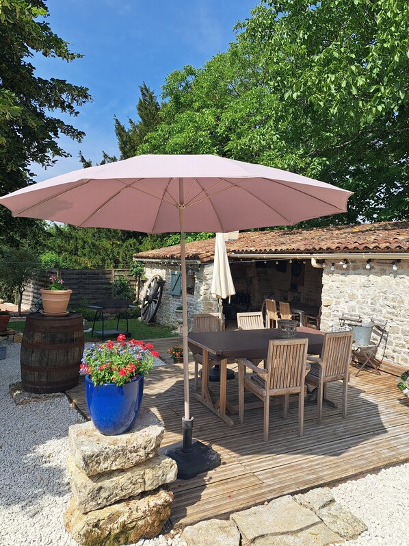 Eine Außenpatio mit Tisch, Stühlen und einem großen Sonnenschirm, im Hintergrund eine Steinmauer.