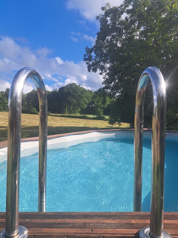 Ein Schwimmbecken mit Metallgeländern, umgeben von einer Holzterrasse und einer Rasenfläche.