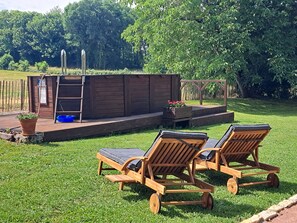 Une terrasse en bois avec une piscine, deux chaises longues et une structure en bois dotée d’une échelle.
