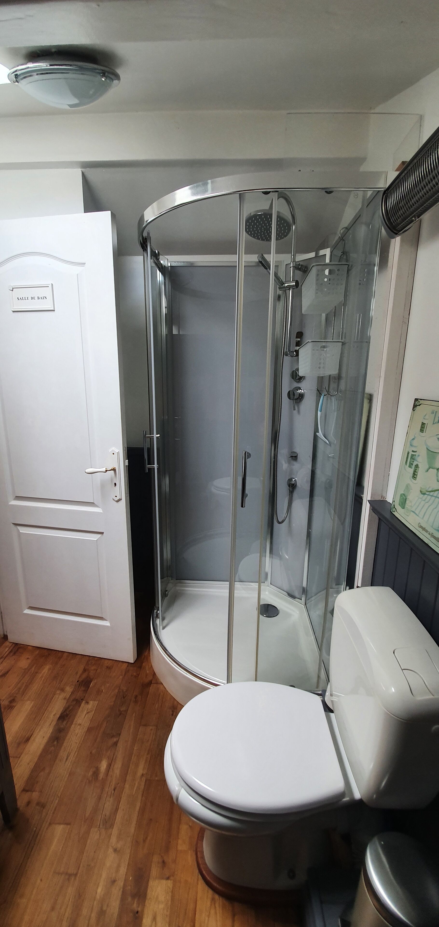 Une salle de bain avec une douche à parois de verre, des toilettes blanches et une porte portant l’inscription « SALLE DE BAIN ».