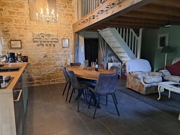 Ein rustikales Interieur mit einer Steinwand, einem Holzesstisch und einer Treppe, die zu einer oberen Ebene führt.