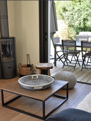 Ein modernes Wohnzimmer mit Kaminofen, einem runden gewebten Korb, einem kleinen Hocker und einem Essbereich mit Stühlen und Tisch.