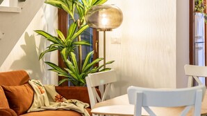 Ein gemütlicher Wohnbereich mit einem braunen Sofa, einem weißen Sessel, einem kleinen Tisch, einer Stehlampe und einer hohen Grünpflanze.