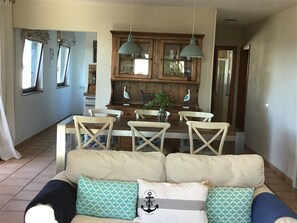 Una sala de estar acogedora con un sofá, una mesa de comedor con sillas y una cocina con armarios de madera y luces colgantes.