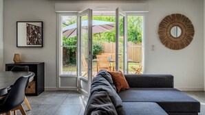 A modern living room with a sectional sofa, a dining table with chairs, and a large window with an umbrella. - Beautiful wooden house with terrace and large garden - Bassin d'Arcachon (Arès)