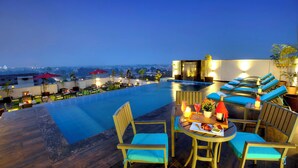 Un espace piscine sur le toit, avec des chaises longues et des tables, un jacuzzi et une vue sur le paysage urbain.