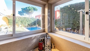 Ein Zimmerwinkel mit Fensterblick auf einen Swimmingpool und einen Garten.