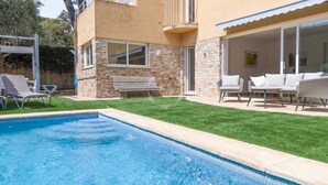 Ein Schwimmbecken mit Steinverkleidung und einer Rasen-Terrasse mit Gartenmöbeln.