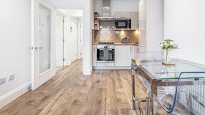 Een moderne keuken met een glazen eettafel, roestvrijstalen apparatuur en een houten vloer.