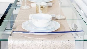 Een moderne keuken met een glazen eettafel, gedekt voor vier personen, met witte borden, kommen en wijnglazen.