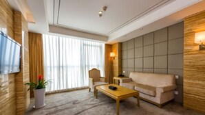 A modern hotel room with a large window, a flat-screen TV, a beige sofa, a wooden coffee table, and a potted plant. - Xiedu Hangchen International Hotel (Chengdu)