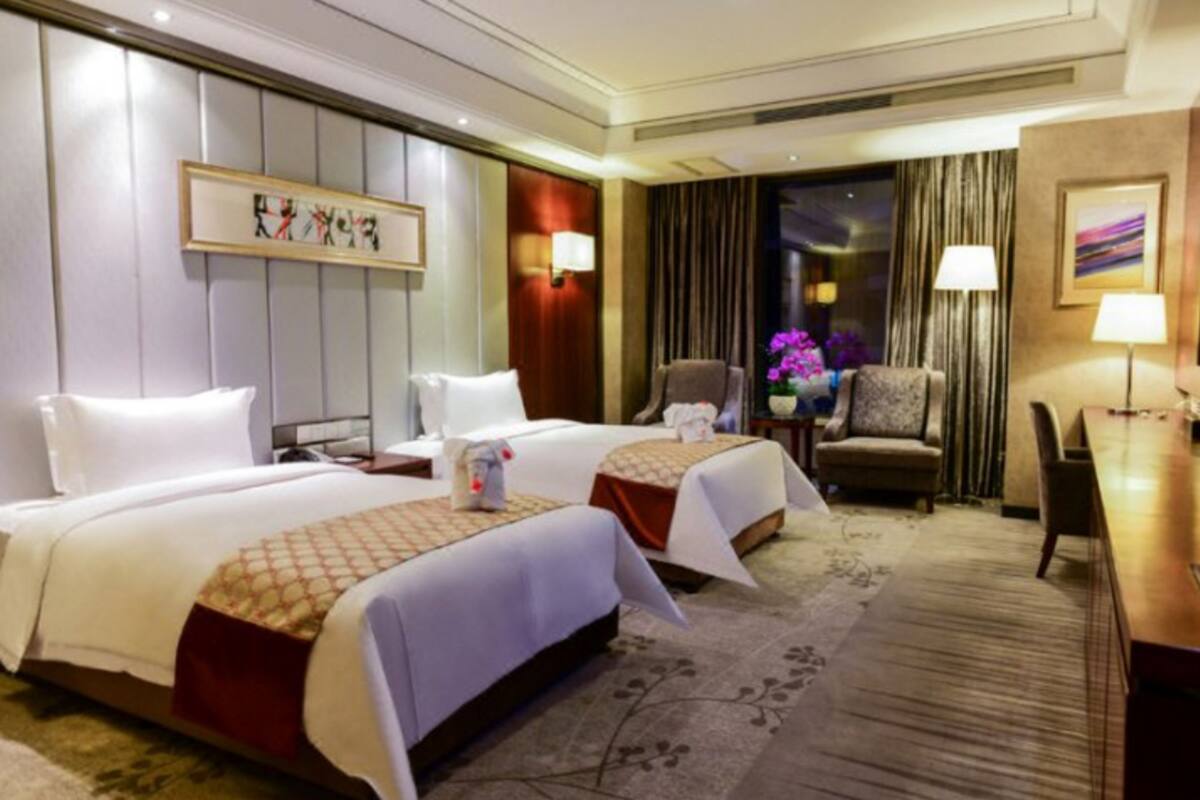 Ein Hotelzimmer mit zwei Betten, einem Schreibtisch, einem Stuhl und Blick auf die beleuchtete Stadt bei Nacht.