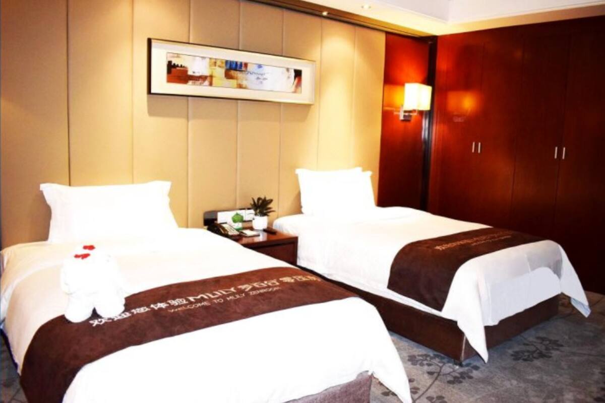 Ein Hotelzimmer mit zwei Betten, einem Nachttisch mit Lampe und einem gerahmten Bild an der Wand.