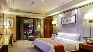 A hotel room with a large bed, a desk, and a chair. There is a painting on the wall and a lamp on the nightstand. - Xiedu Hangchen International Hotel (Chengdu)