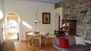 Un salon chaleureux avec un mur en pierre, un coin repas avec une table et des chaises, et un canapé gris agrémenté de coussins rouges.