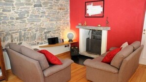 Un salon chaleureux avec deux canapés gris, un mur en pierre, un mur d’accent rouge, une cheminée et une petite étagère sur laquelle sont posés un globe terrestre et une lampe.