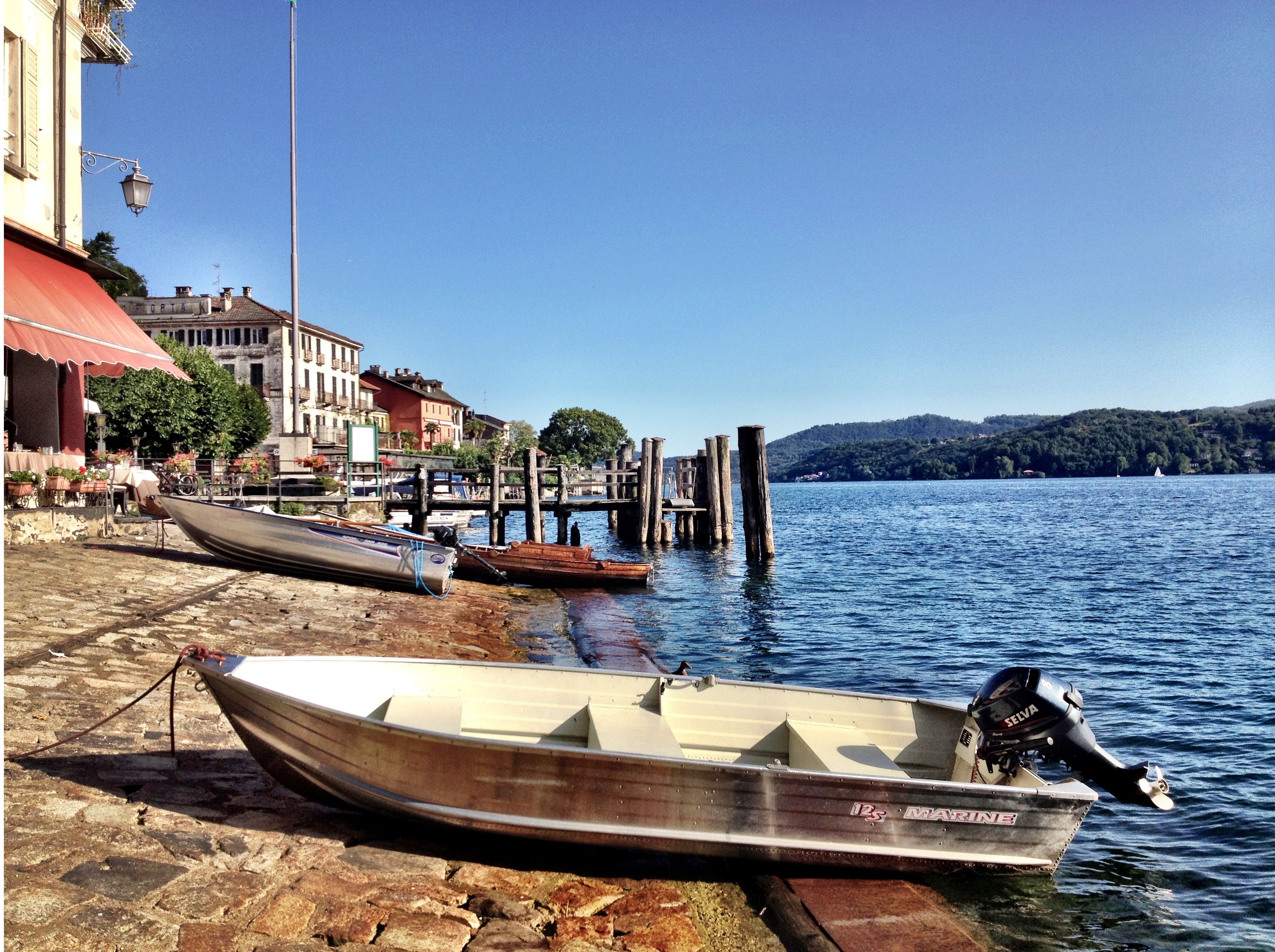 A waterfront scene with boats docked at a pier, a stone walkway, and buildings in the background.