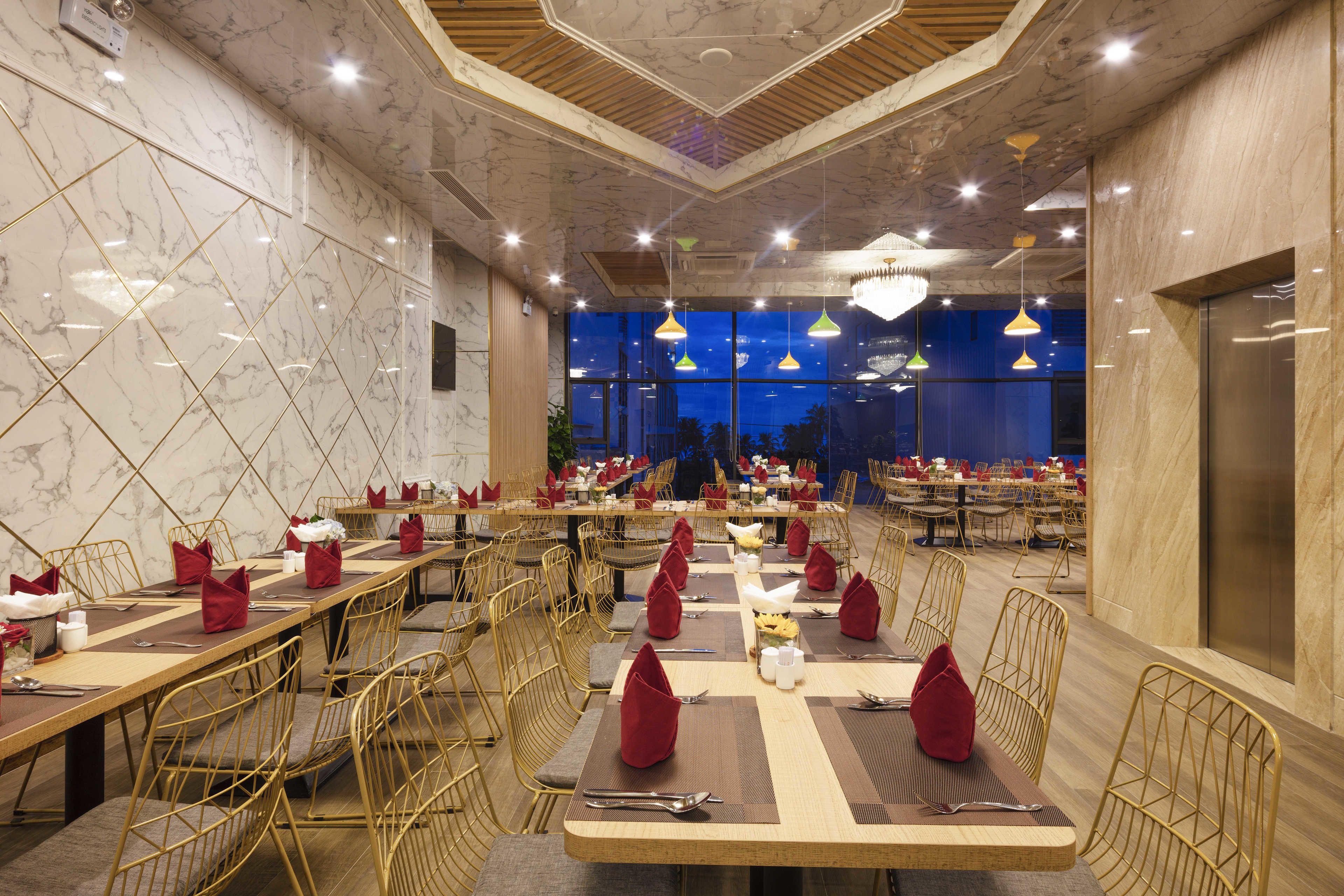 A spacious restaurant with marble walls, multiple dining tables, and golden chairs.