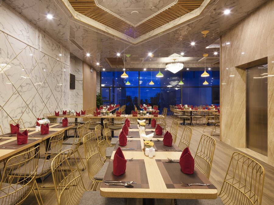 A spacious restaurant with marble walls, multiple dining tables, and golden chairs.