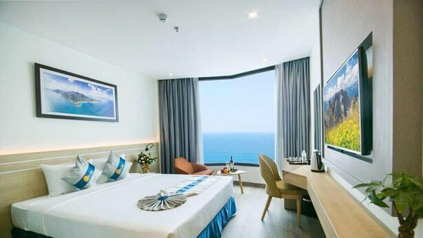 Habitación de hotel con una cama grande, un escritorio, una silla, un televisor y vistas al mar.