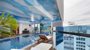 Una piscina infinita en el interior con sillones de descanso, vista a la ciudad y un mural en el techo.