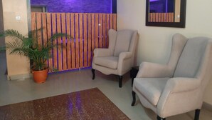 A room with two armchairs, a potted plant, a wooden partition with vertical stripes, and a mirror on the wall. - The Capital Apartments (Abuja)