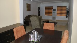 A dining area with a dark wooden table, four chairs, and two metallic candle holders. - The Capital Apartments (Abuja)