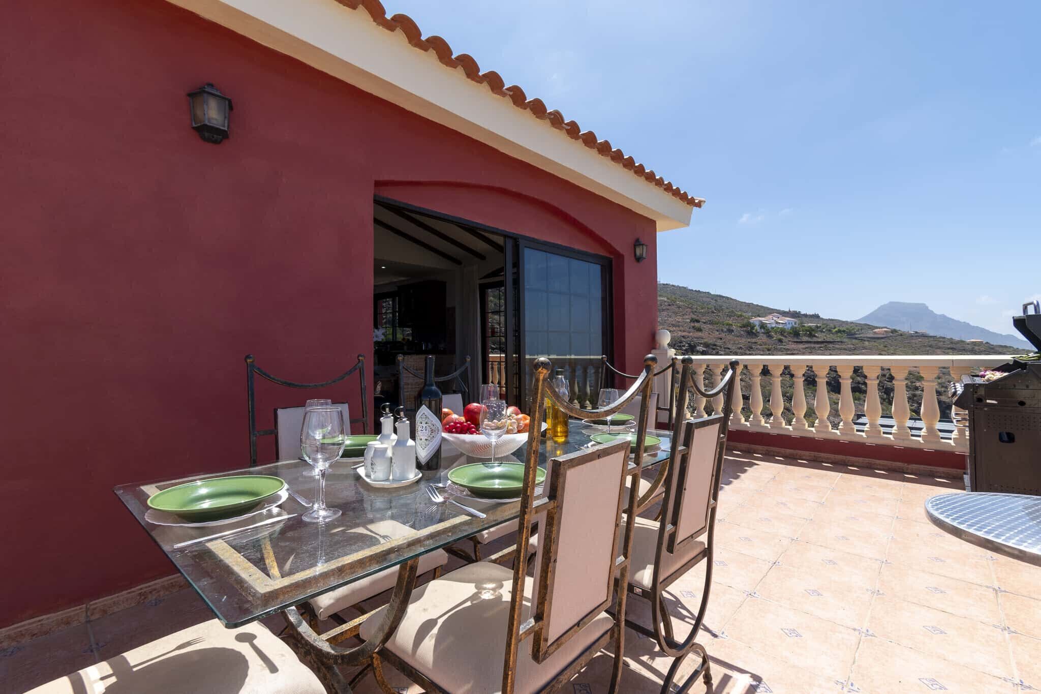 A dining table set with plates, glasses, and condiments on a terrace with a view of a mountain.