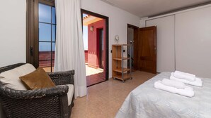 Ein Hotelzimmer mit einem Bett, einem Korbstuhl, einem kleinen Regal und Blick ins Freie.