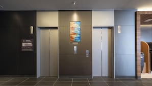 A modern elevator with a digital display, emergency instructions, and a colorful artwork above it. - Washington R&B Hotel Nagoya Shinkansenguchi (Nagoya)